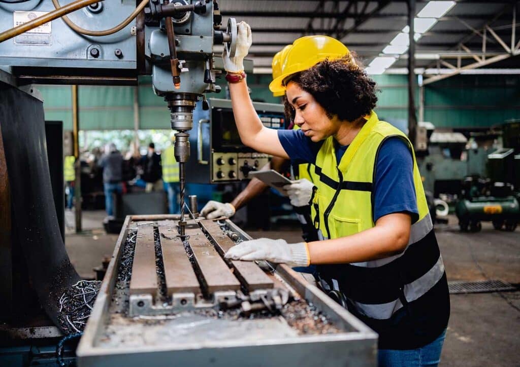 Women workers or mechanics in safety uniforms are working on metal drilling machines